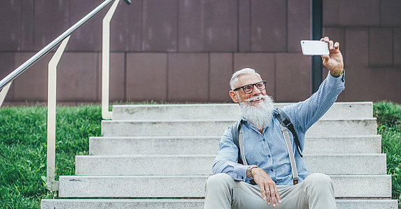 Ein älterer Herr mit Bart und Brille macht ein Selfie mit einem Smartphone