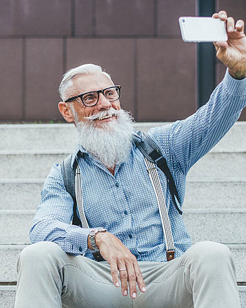 Ein älterer Herr mit Bart und Brille macht ein Selfie mit einem Smartphone