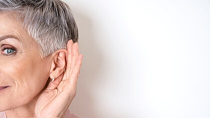 Eine ältere Dame hält die Hand hinterm Ohr