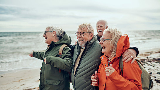 Eine Gruppe älterer Damen und Herren am Strand mit Windjacken