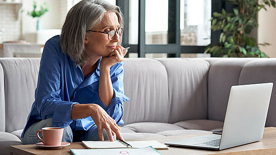 Ältere Dame mit Brille sitzt vor ihrem Laptop