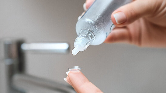 Pflegemittel wird auf eine Kontaktlinse getropft