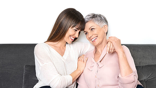 Eine ältere und eine junge Dame sitzen gemeinsam auf einem Sofa